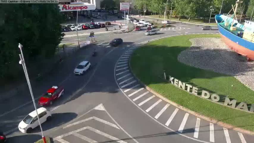 A sunny day shows a roundabout with several cars driving around it, near a large ship statue and some parked cars.