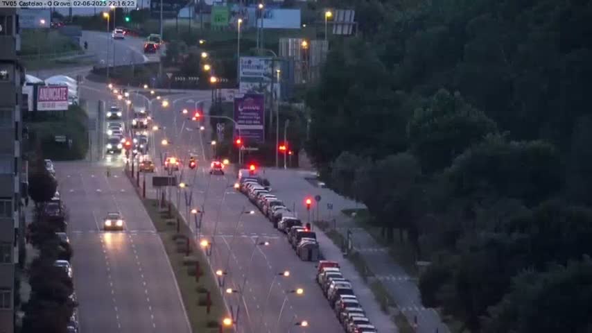 A multi-lane road with cars driving in both directions at dusk, lined with trees and streetlights.