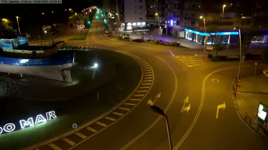 At night, a roundabout near a body of water features a large model boat, illuminated by streetlights.