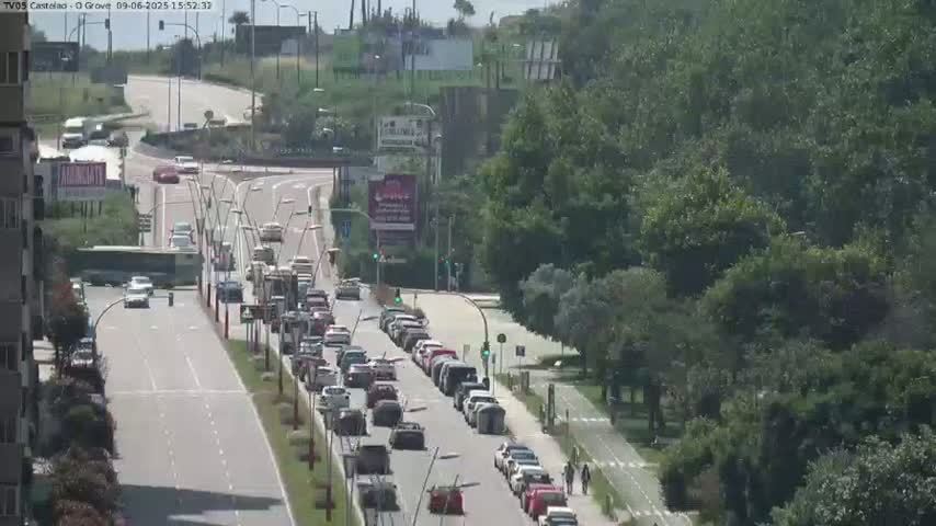 A sunny day shows a highway intersection with multiple lanes of cars driving in both directions, surrounded by green trees and a bike path.