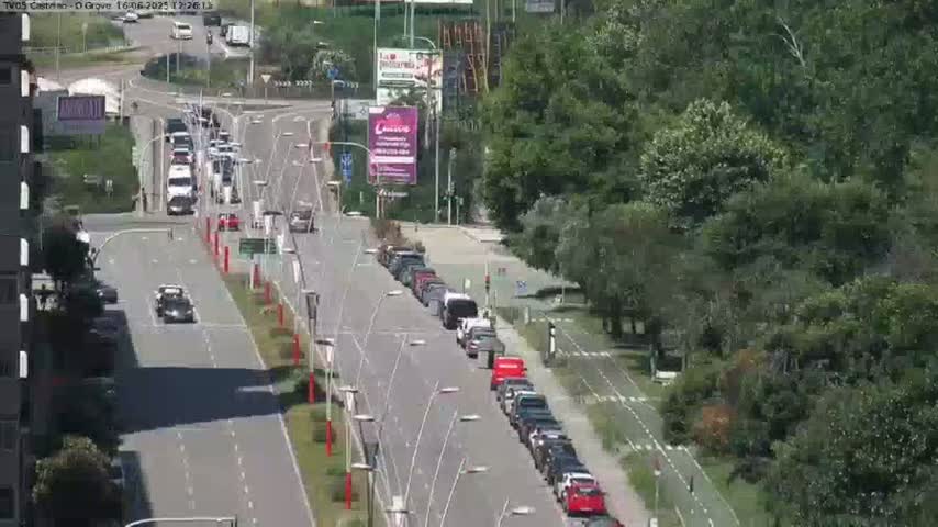 A high-angle view shows a sunny day with several cars driving on a multi-lane road that curves through a lush green area with a bike path.