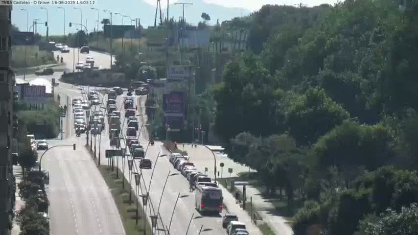 A sunny day shows a multi-lane road with heavy traffic, flanked by lush green trees and hills.