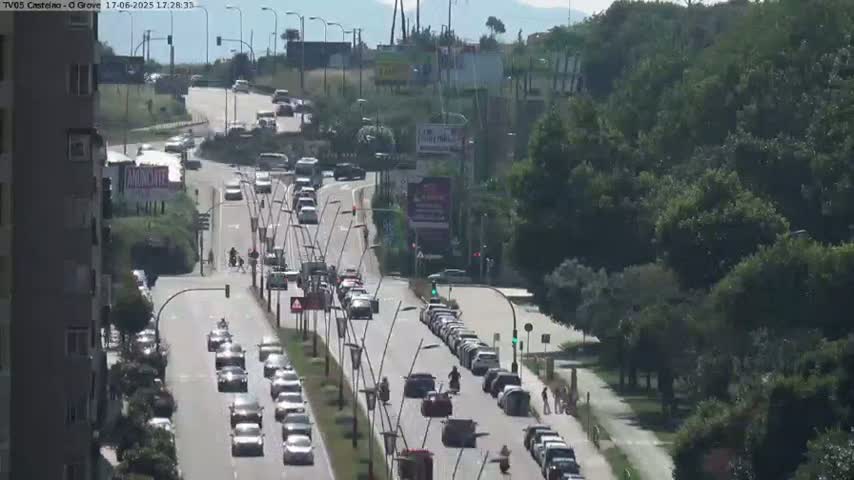 A sunny day overlooking a multi-lane road with moderate traffic, lined with trees and buildings.