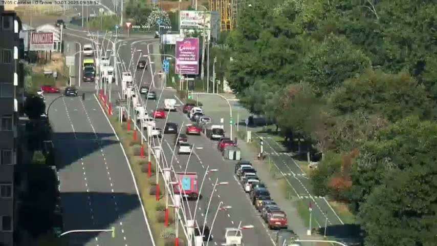 A multi-lane road with moderate traffic flows through a lush, green landscape on a sunny day.