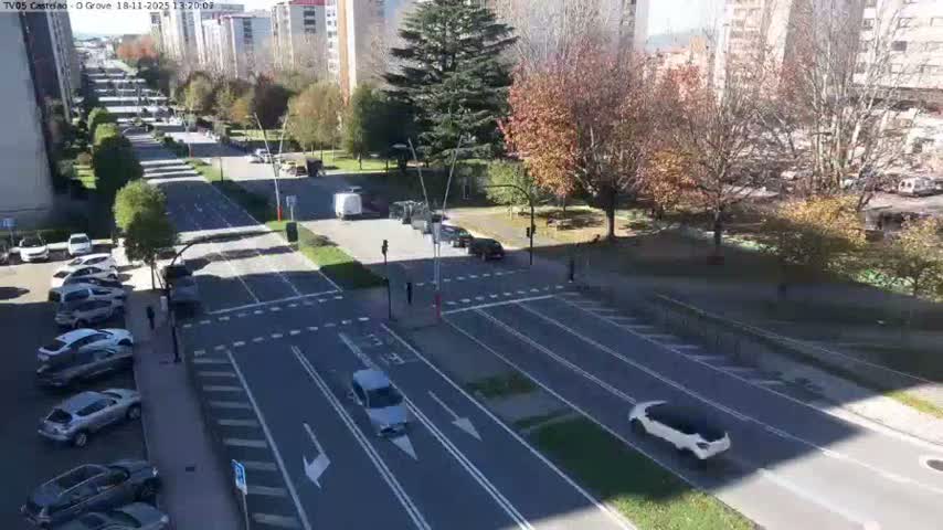 An elevated view captures a multi-lane urban road and intersection at night, with wet surfaces brightly reflecting streetlights and vehicle lights under rainy conditions.