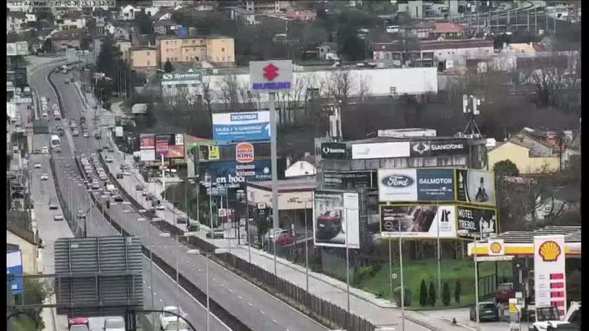 A highway with moderate traffic flows through a city with numerous billboards and buildings on an overcast day.