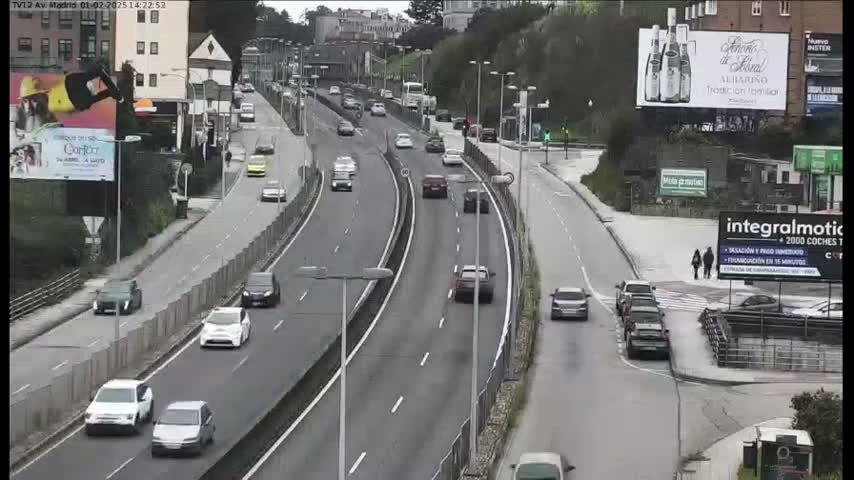 A multi-lane highway curves through a city, with cars driving in both directions on a mostly cloudy day.