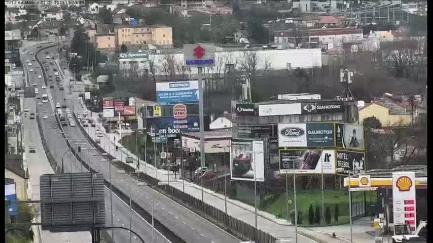 A highway with moderate traffic flows through a city area with numerous billboards and buildings on either side, under an overcast sky.