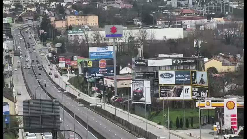 A highway with moderate traffic flows past billboards and businesses on an overcast day.