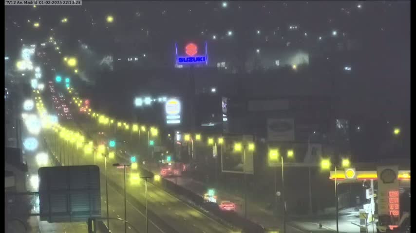 A rain-swept highway at night shows traffic lights and the lights of buildings and vehicles, with a Suzuki sign visible in the distance.