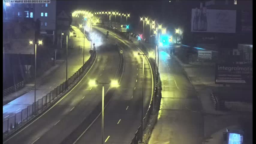 A rain-slicked highway at night is illuminated by streetlights, with a few vehicles visible on the road.