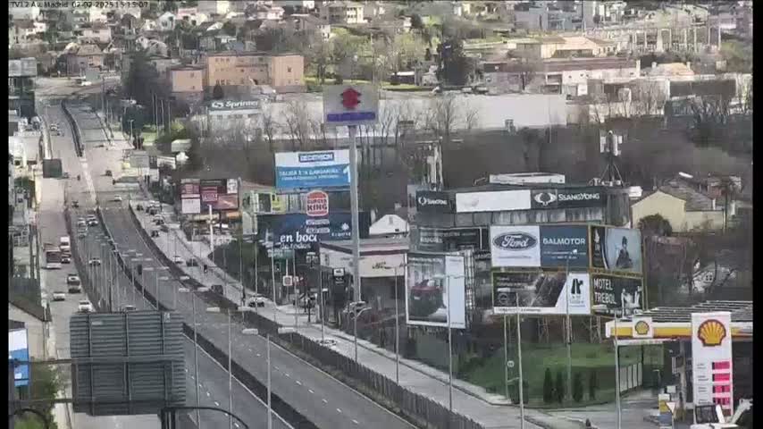 A highway scene with moderate traffic is shown on an overcast day, surrounded by buildings and billboards.