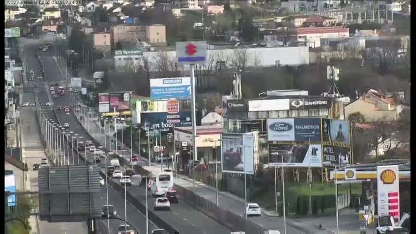 A multi-lane highway with moderate traffic flows through a city under a mostly clear sky.