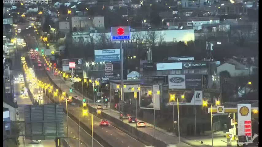 A nighttime, slightly overcast view of a busy highway with moderate traffic, lined with businesses and illuminated by streetlights.