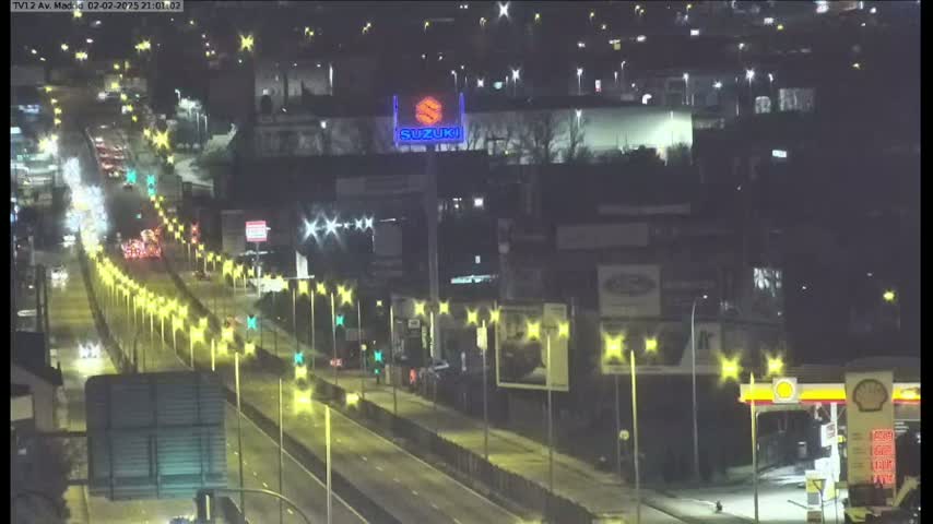 A nighttime, wet highway scene shows multiple lanes of traffic with illuminated streetlights and a Suzuki sign visible in the distance.