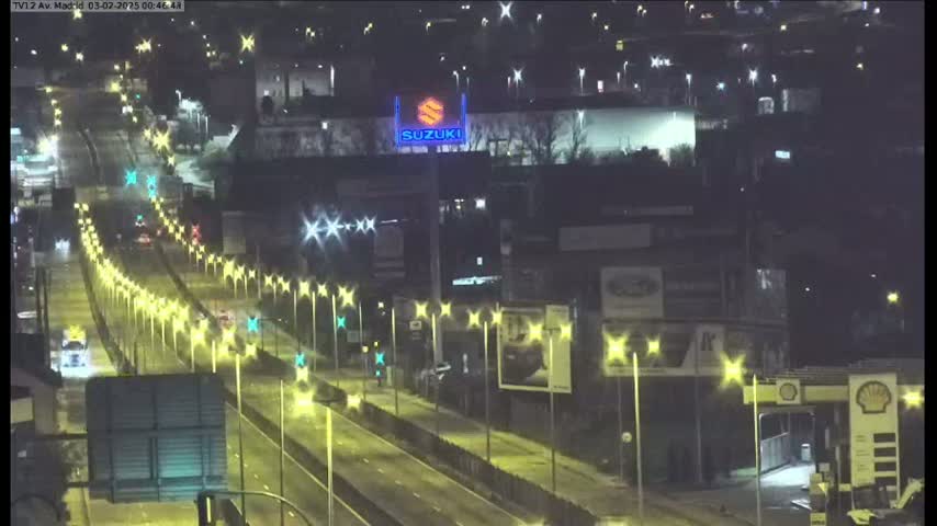 A nighttime, brightly lit highway scene shows several vehicles traveling on a multi-lane road, flanked by streetlights and buildings.