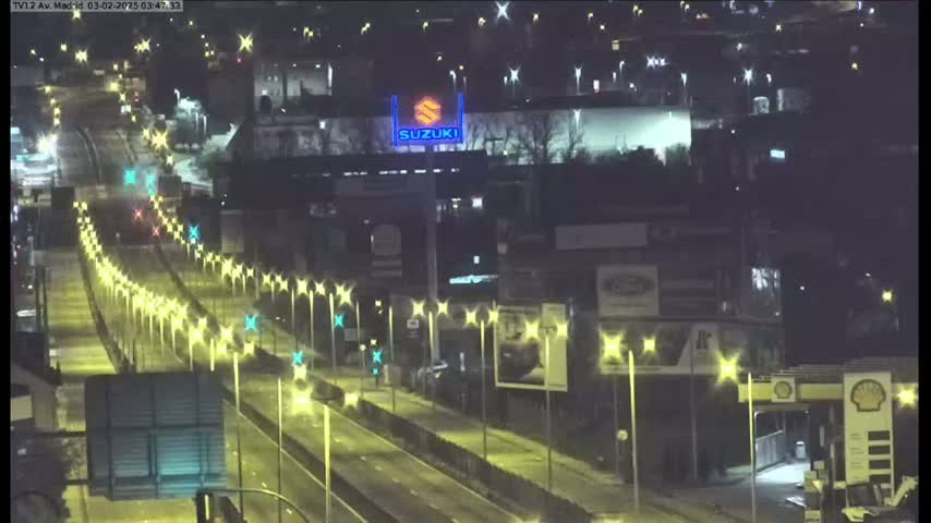 A nighttime, illuminated view of a multi-lane highway, lined with streetlights, passing by commercial buildings.