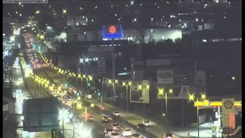 A nighttime, aerial view of a heavily congested highway with many streetlights and a Suzuki billboard visible in the distance.