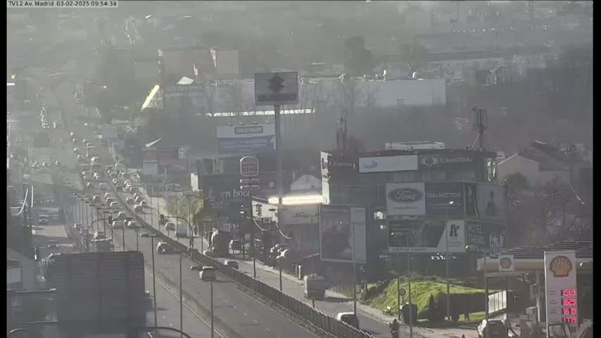 A hazy, sunny day reveals a busy highway with moderate traffic, flanked by buildings with numerous billboards.
