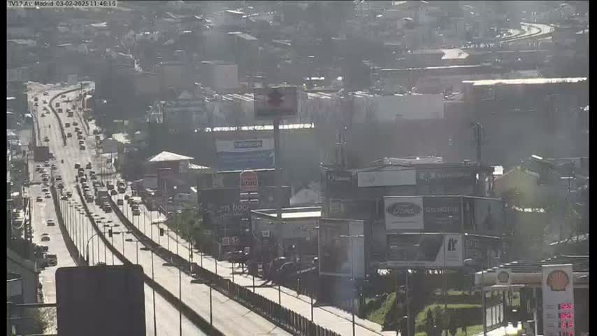 A hazy, sunny day reveals a highway with moderate traffic flowing through a city with numerous buildings and billboards.