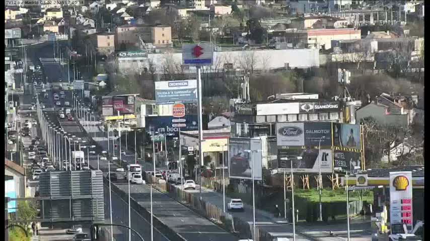 A highway with moderate traffic flows through a city under a sunny sky, surrounded by buildings and billboards.