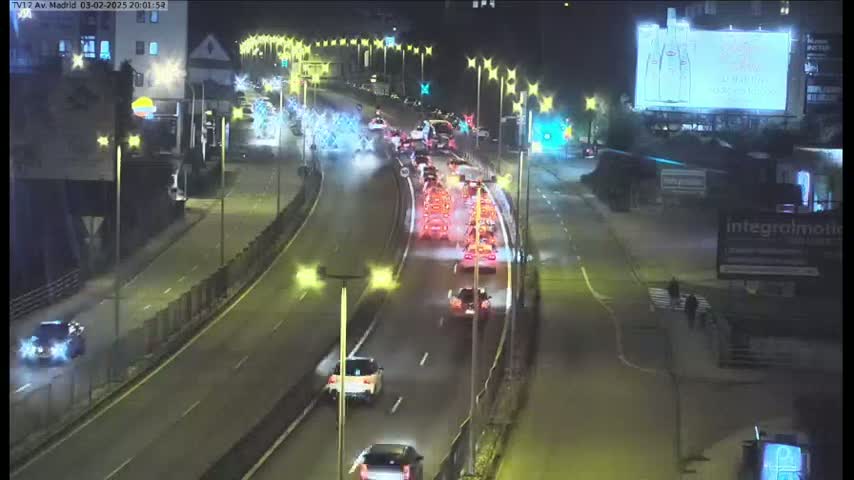 A nighttime overhead view shows a highway with moderate traffic flowing under illuminated streetlights and holiday decorations.