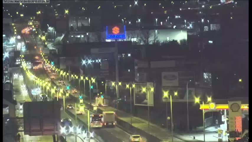 A nighttime, brightly lit highway scene shows heavy traffic flowing under streetlights and past a Suzuki dealership sign.