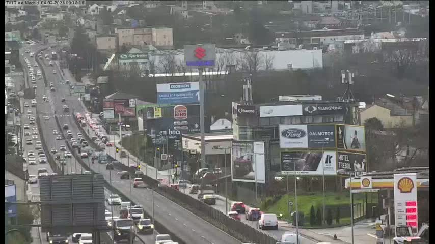 A multi-lane highway with heavy traffic flows through a city on an overcast day.
