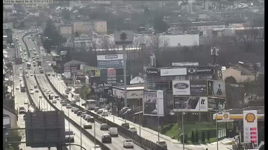A highway with moderate traffic flows through a city on a sunny day, passing numerous billboards and buildings.