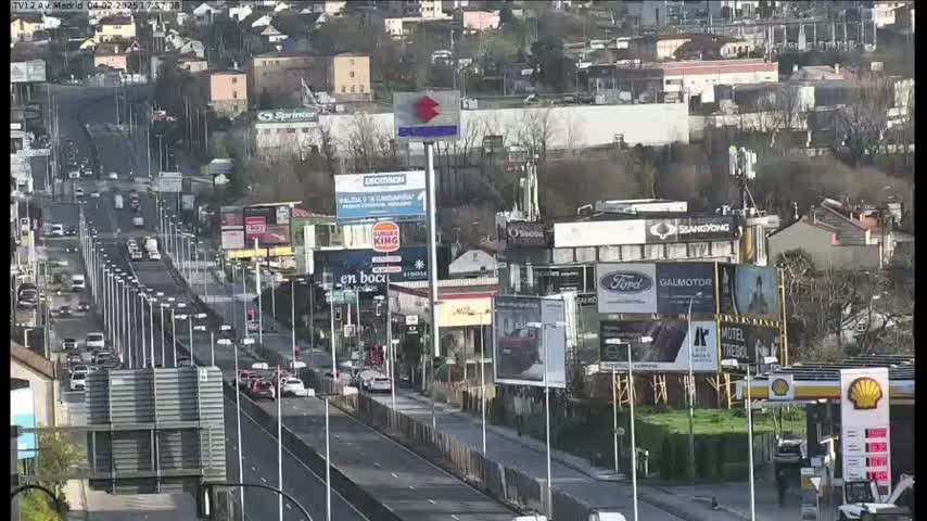 A multi-lane highway with moderate traffic flows through a city, under a partly cloudy sky.