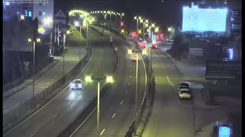 A nighttime view of a multi-lane highway with several cars driving on it, under artificial light from streetlamps.
