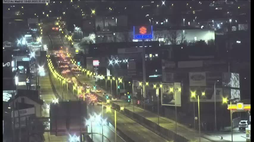 A nighttime aerial view shows a multi-lane highway congested with traffic under illuminated streetlights.