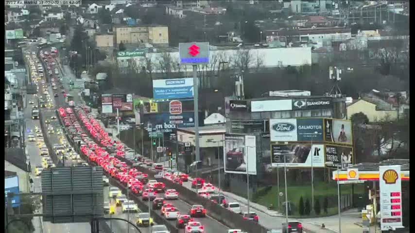 A heavily congested highway stretches through a city on an overcast day, with numerous billboards lining the roadside.