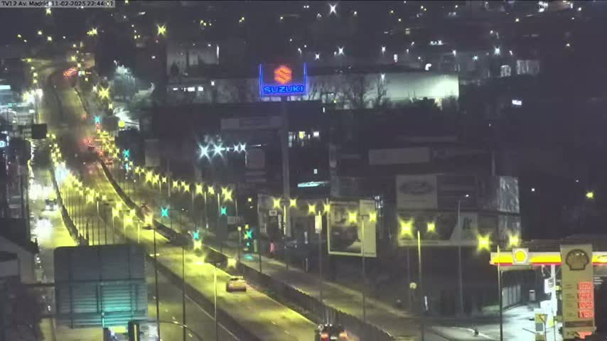 A nighttime, wet highway scene shows a multi-lane road with cars driving under bright streetlights.