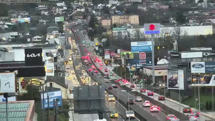 A highway with heavy traffic flows through a city under overcast skies.