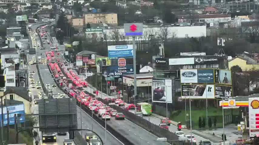 A long line of slow-moving traffic stretches along a multi-lane highway in an urban area on an overcast day.