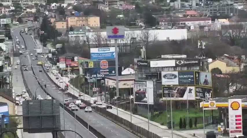 A highway with moderate traffic flows through a city on an overcast day, with numerous billboards and buildings lining the roadside.