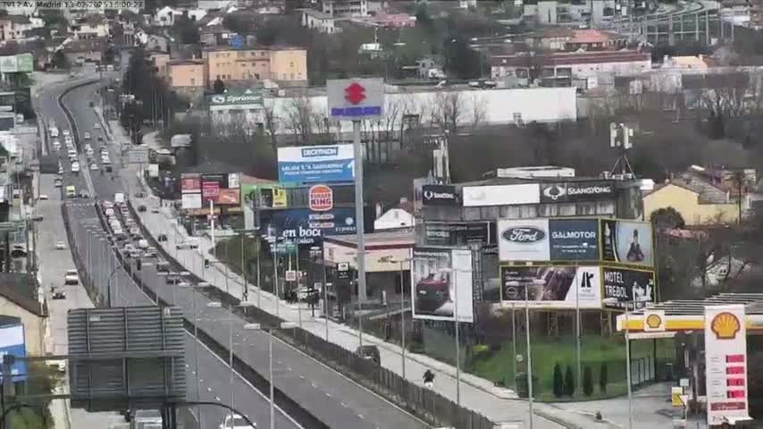 A highway with moderate traffic flows through a city, under a cloudy sky.