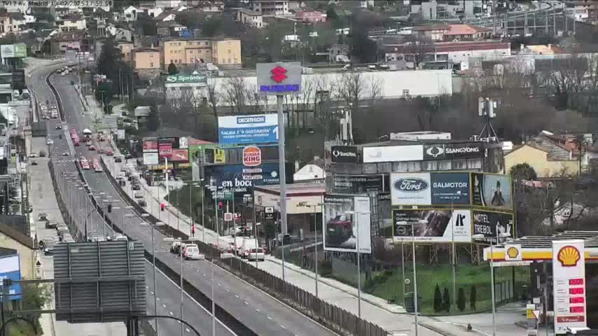 A highway scene with moderate traffic, numerous billboards, and buildings lining both sides of the road on a mostly clear day.