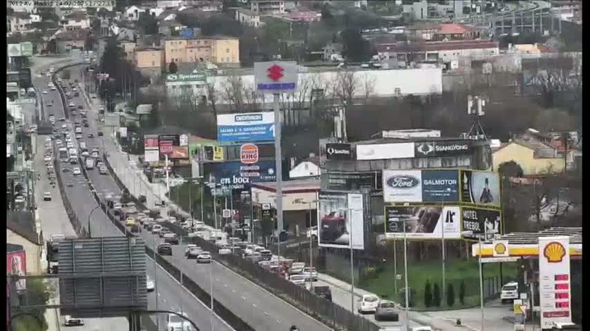A highway scene with moderate traffic under a partly cloudy sky shows many billboards and businesses lining the road.