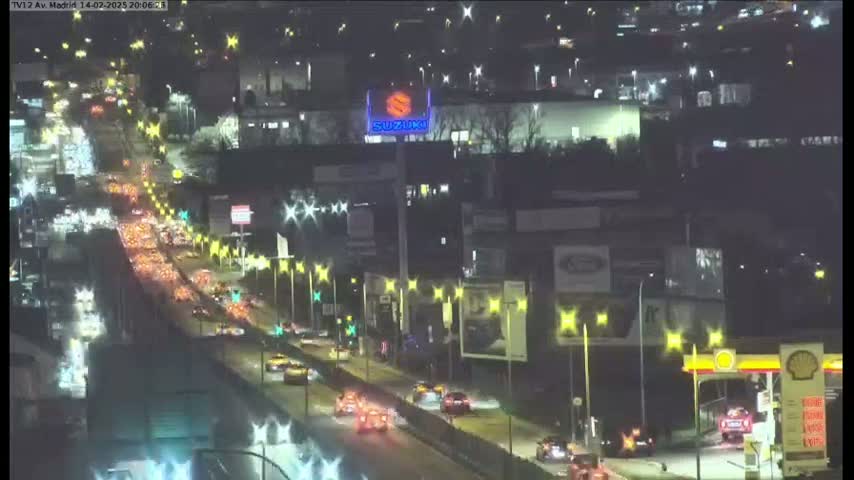 A nighttime, congested highway scene shows numerous vehicles traveling along a multi-lane roadway, under illuminated streetlights.