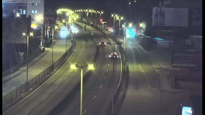A nighttime view of a multi-lane highway with several cars driving, illuminated by streetlights.