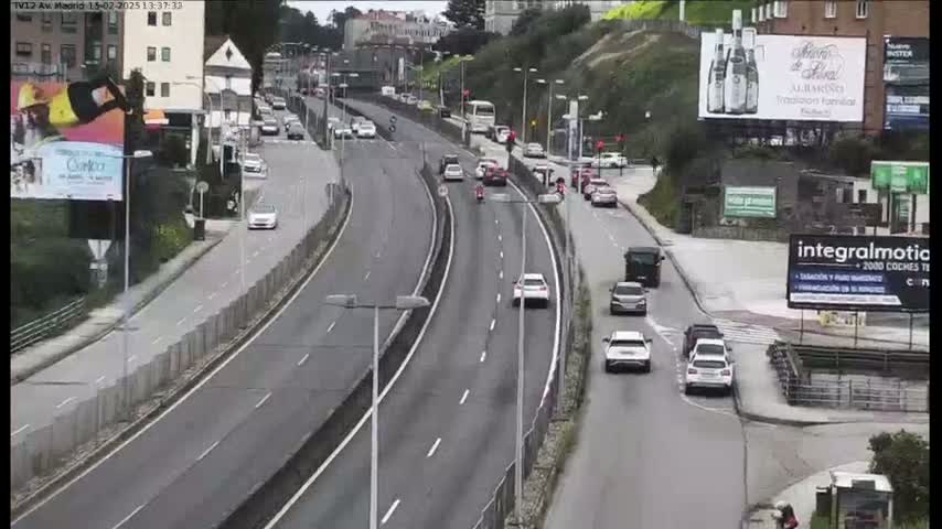 A multi-lane highway curves gently through a cityscape, with cars and a bus traveling in both directions on a mostly clear day.