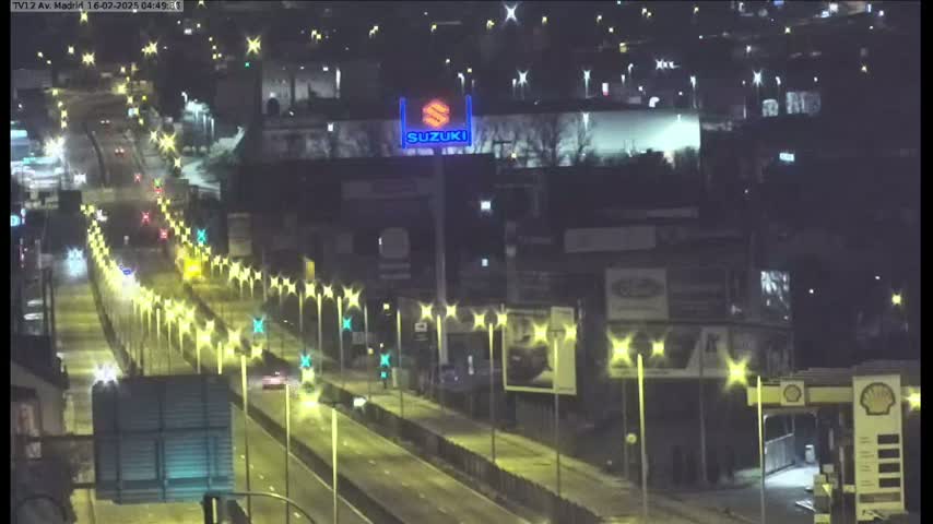 A nighttime view of a multi-lane highway with sparse traffic, lined with illuminated streetlights, and buildings with advertisements visible in the background.