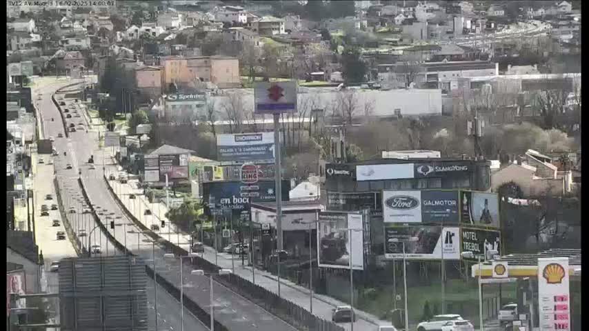A highway with moderate traffic flows through a town on a sunny day, surrounded by buildings and billboards.
