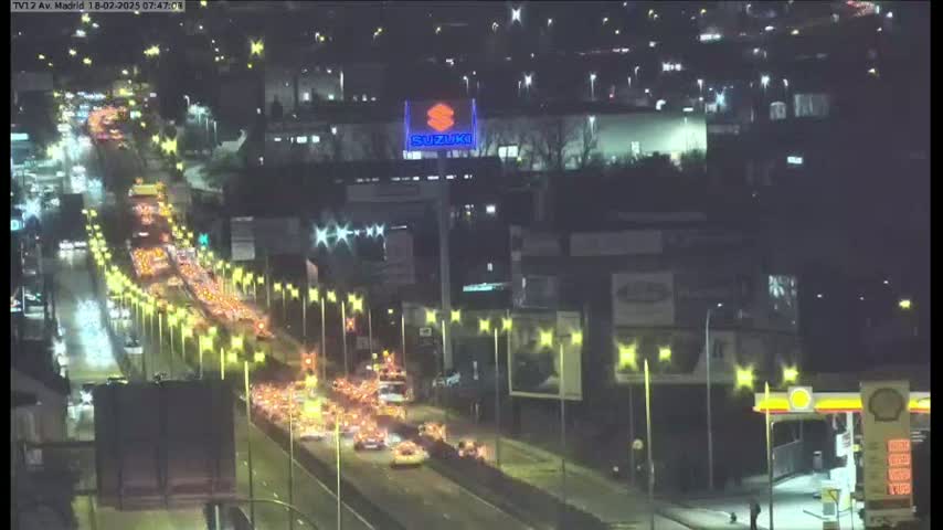 A nighttime aerial view shows a heavily congested highway with many cars and lights under wet conditions.