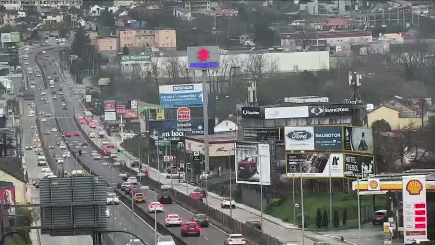 A highway scene shows moderate traffic moving in both directions, with numerous billboards and buildings lining the roadside on an overcast day.