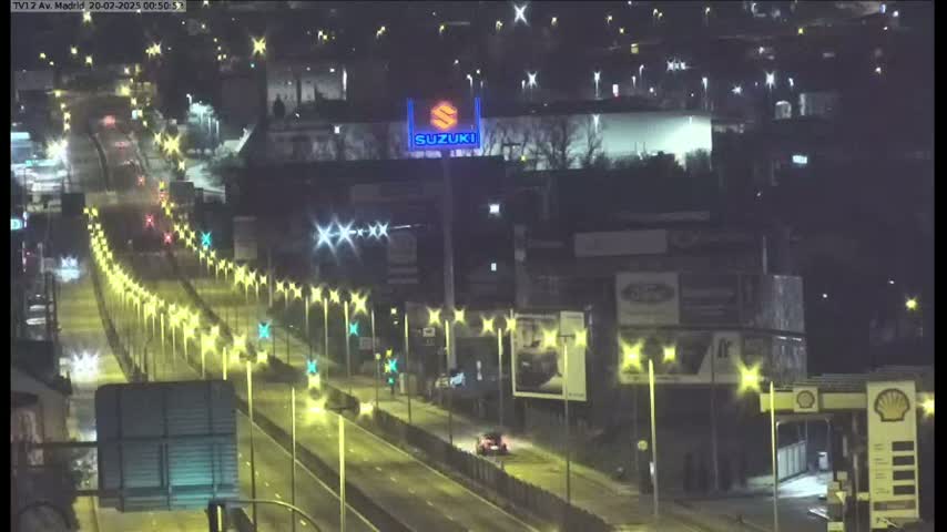 A nighttime, dimly lit highway scene with several vehicles traveling along multiple lanes, lined with streetlights and billboards, including a large Suzuki advertisement.