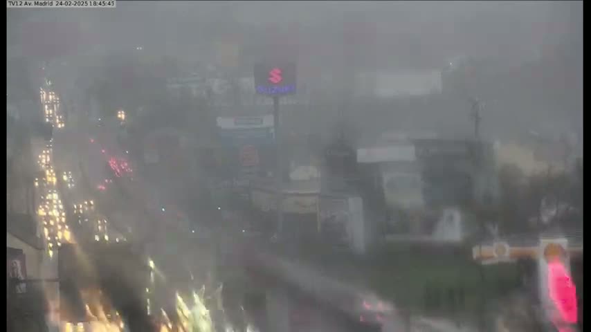 A hazy, heavy rain obscures a view of a busy highway and buildings at dusk.