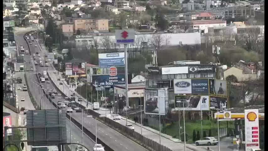 A multi-lane highway with moderate traffic flows through a city landscape on a partly cloudy day.